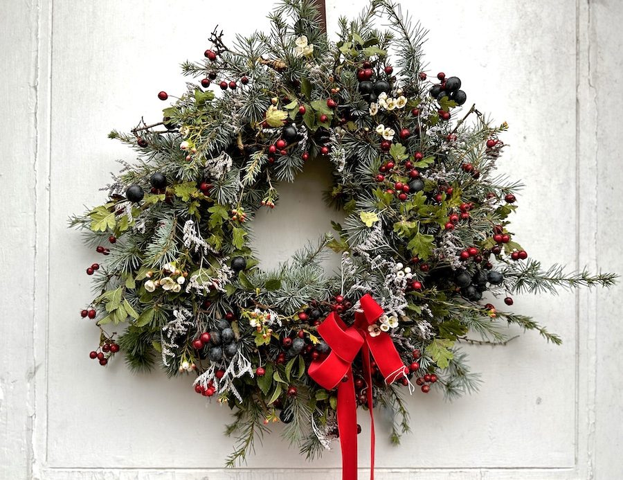 Berry Christmas Wreath is displayed on a white door. It includes winter foliages and mixed red berries with a red bow.